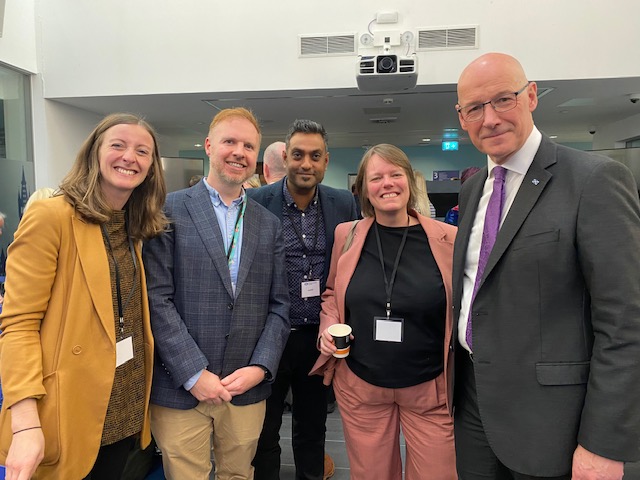A photo of five people at an event. From left to right: Sara Redmond (The Alliance), Nick Ward (Change Mental Health), Tejesh Mistry (Voluntary Health Scotland), Rachel Cackett (CCPS) and John Swinney (First Minister)
